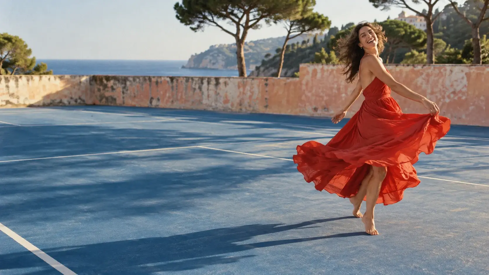 A dancer in a vermilion dress turns on a sunlit blue court